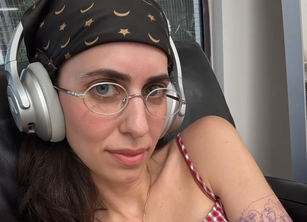 Hila Klein in a hot tub wearing headphones and a checkered top.