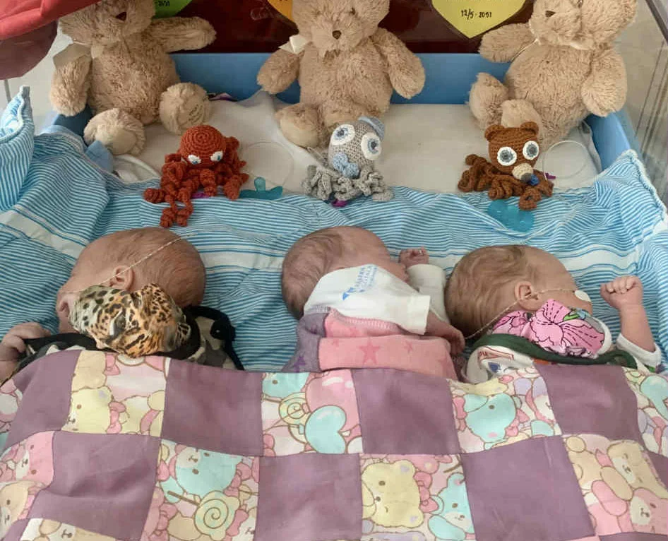 Three teddy bears and toys with blankets set up in cot.