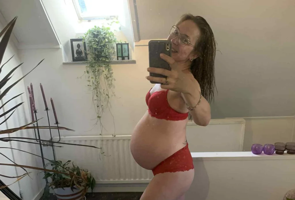 Pregnant woman in red bikini posing in bathroom mirror selfie.