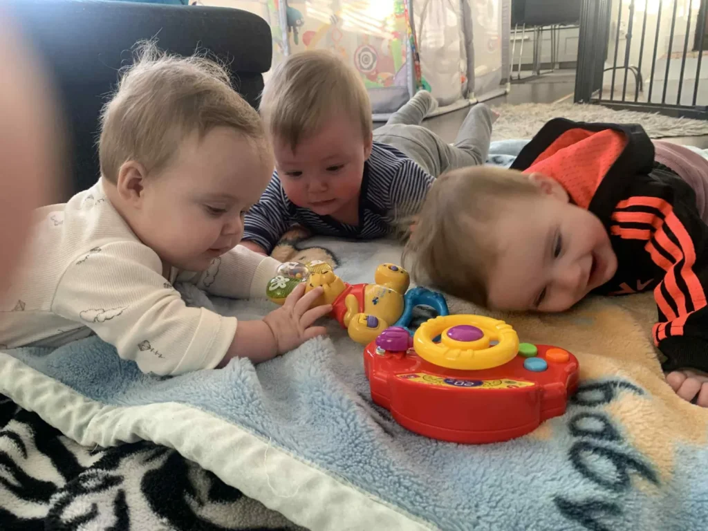 Three toddlers playing with toys on activity mat.