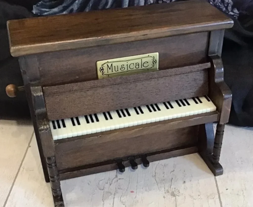 Wooden miniature wind-up piano with dark stain and ivory keys, labelled Musicale