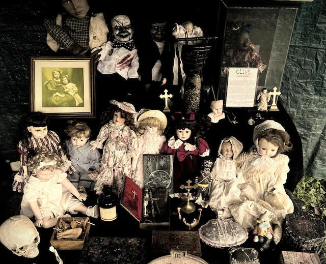 Shelf display of multiple haunted dolls including figures in various dress styles and colours