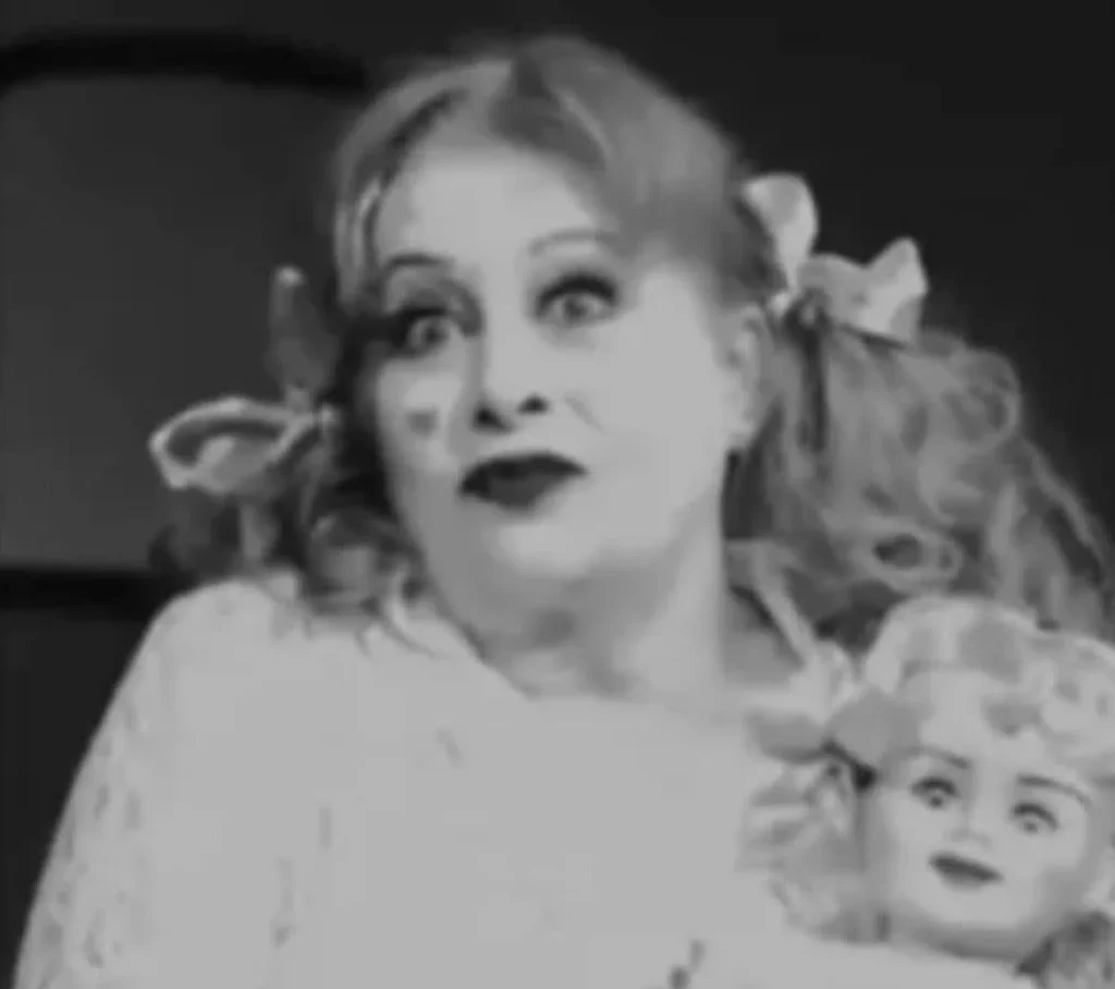 Blonde doll with raised arms wearing white lace dress displayed against dark background