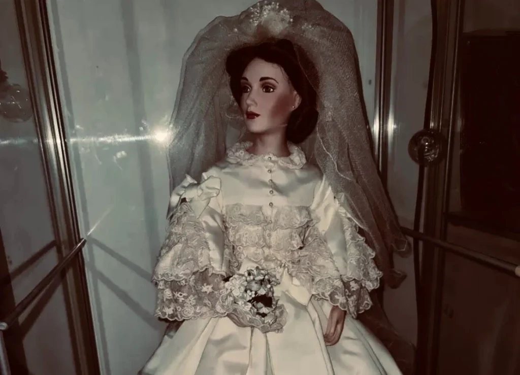 Life-size bride doll in white wedding dress with veil and reddish-brown hair inside glass case