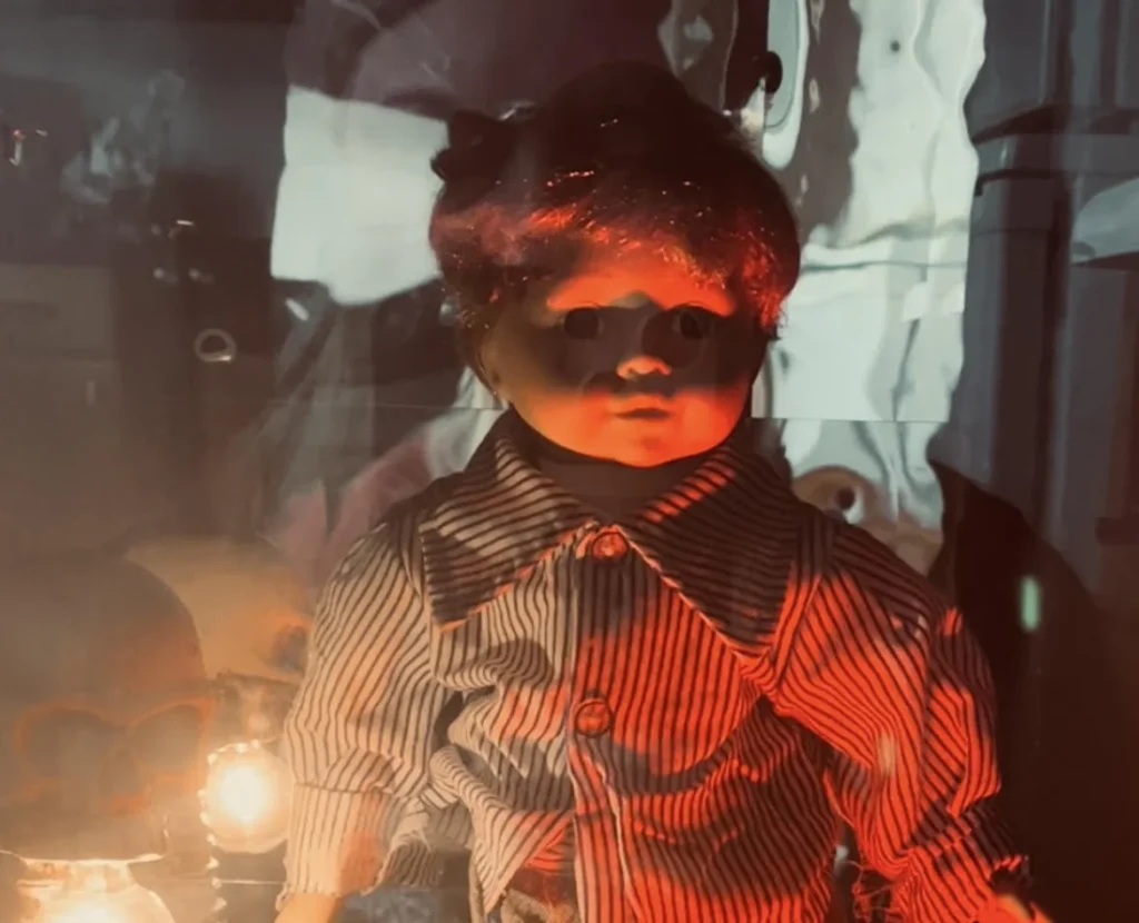 Doll with blonde hair and blue eyes wearing striped shirt inside illuminated glass display box